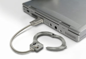 Closed-up gray laptop with a HDMI connector and that is connected with a handcuff that means criminal fraud Western Australia in which Criminal Lawyers Perth can help you.