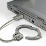 Closed-up gray laptop with a HDMI connector and that is connected with a handcuff that means criminal fraud Western Australia in which Criminal Lawyers Perth can help you.
