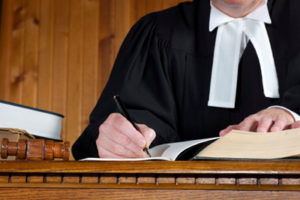 A judge sitting and writing on a paper which is placed on top of a wooden table, which is part of "choosing a criminal lawyer blog".