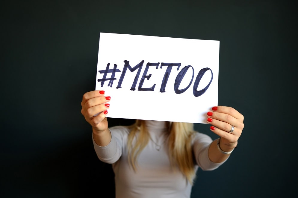 Closed-up of a word written on a white board that says "#METOO", which is being held by a woman that represents cases about historical sex abuse.